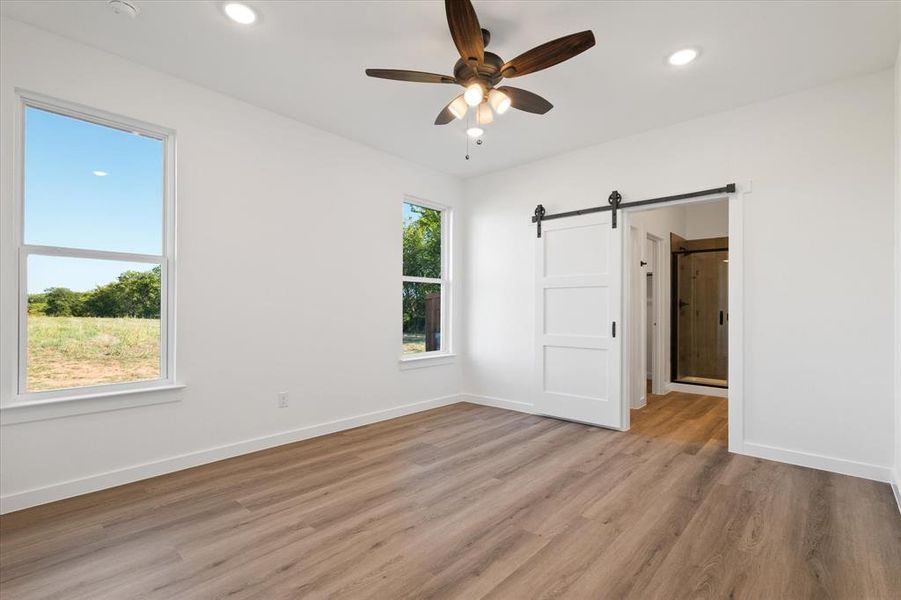 Empty room with ceiling fan, light hardwood / wood-style floors, and a barn door