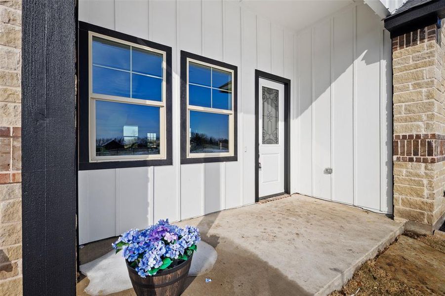 Exterior featuring board and batten siding, stone facade, black trim windows, a decorative glass entry door, and a concrete porch Exterior featuring board and batten siding, stone facade, black trim windows, a decorative glass entry door, and a concrete porch