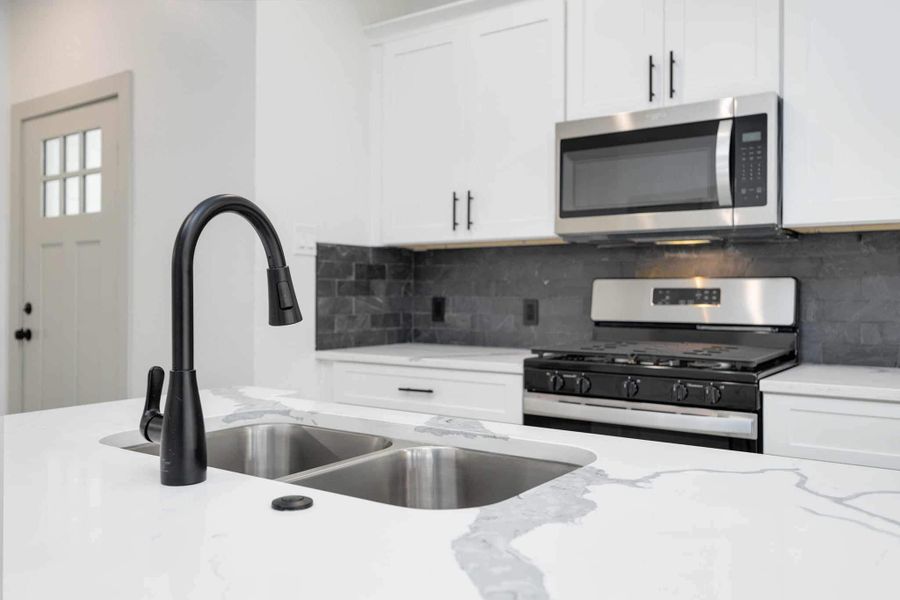 Large island with dual stainless steel sink, matte black pull-down faucet, and elegant quartz countertops with soft gray veining. Perfect for entertaining or everyday cooking.