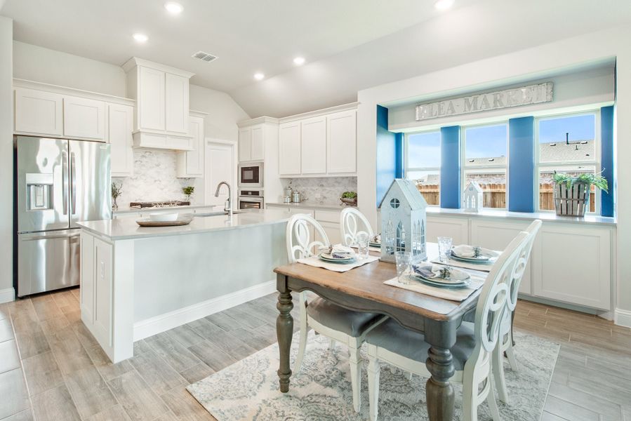 Open kitchen and dining area with white cabinets, large island, stainless appliances, and a four-seat dining table near a bay window.