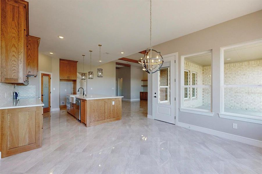 Kitchen with decorative light fixtures, decorative backsplash, light tile patterned floors, and a center island with sink