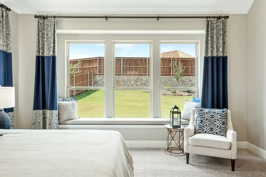 Bedroom with triple windows, built-in window seat, blue curtains, and backyard view