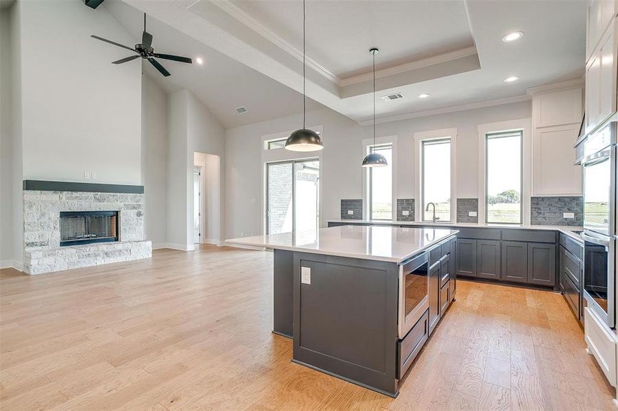 Kitchen with a stone fireplace, a center island, hanging light fixtures, white cabinetry, and light hardwood / wood-style flooring