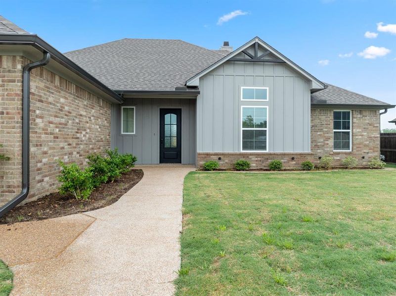 View of front of house with board and batten siding, brick siding, a shingled roof, and a front yard View of front of house with board and batten siding, brick siding, a shingled roof, and a front yard
