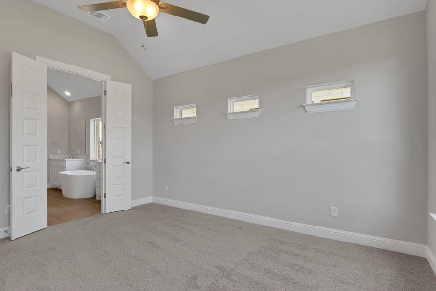 Unfurnished bedroom featuring baseboards, ensuite bathroom, carpet floors, visible vents, and lofted ceiling