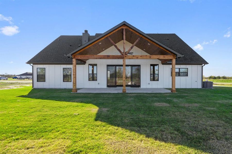 Rear view of house featuring board and batten siding, a patio, a chimney, and roof with shingles Rear view of house featuring board and batten siding, a patio, a chimney, and roof with shingles