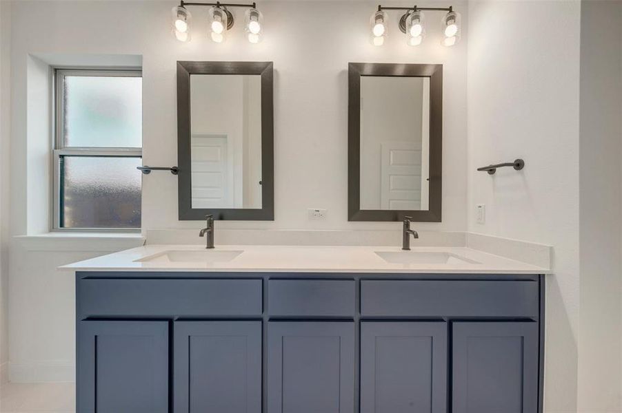 Dual vanity with white countertop and integrated sinks, complemented by two framed mirrors and two three-bulb light fixtures