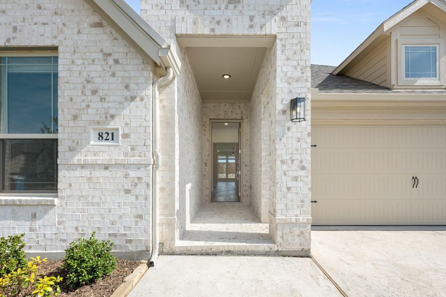 Home entrance with covered brick entryway, wall lantern, and single-car garage beside front door Home entrance with covered brick entryway, wall lantern, and single-car garage beside front door