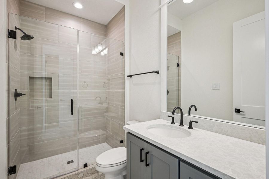 Modern bathroom featuring a spacious glass-enclosed shower with sleek fixtures, a stylish vanity with a marble countertop, and elegant lighting.