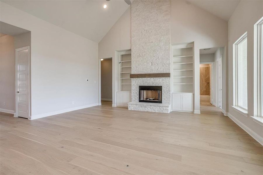 Unfurnished living room with light hardwood / wood-style floors, a stone fireplace, high vaulted ceiling, and built in features