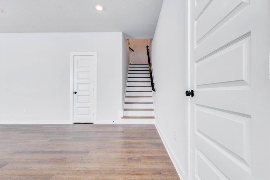 A clean, minimalistic view of the staircase and hallway reveals contemporary finishes like matte black hardware, square-trim doors, and smooth white walls. This transitional space connects the downstairs open living to the upstairs bedrooms and game room retreat.