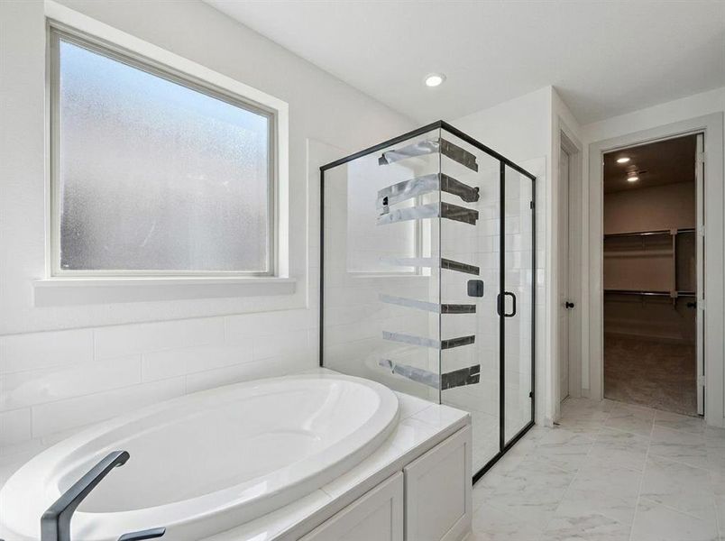 Bathroom featuring a built-in soaking tub with a dark-finish faucet, a frameless glass shower enclosure with dark trim, and white subway tile wainscoting