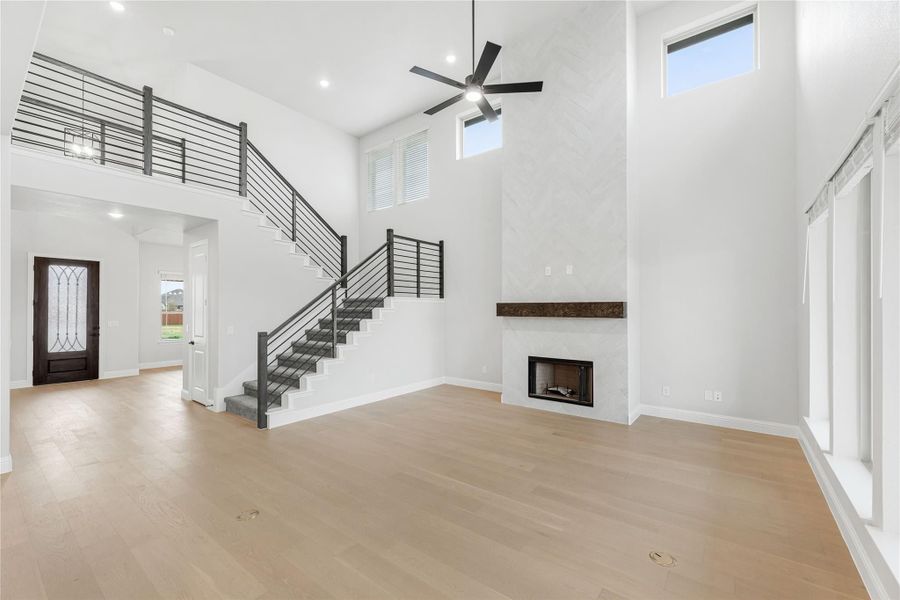 Open living room with two-story ceiling, fireplace, staircase, and light hardwood floors