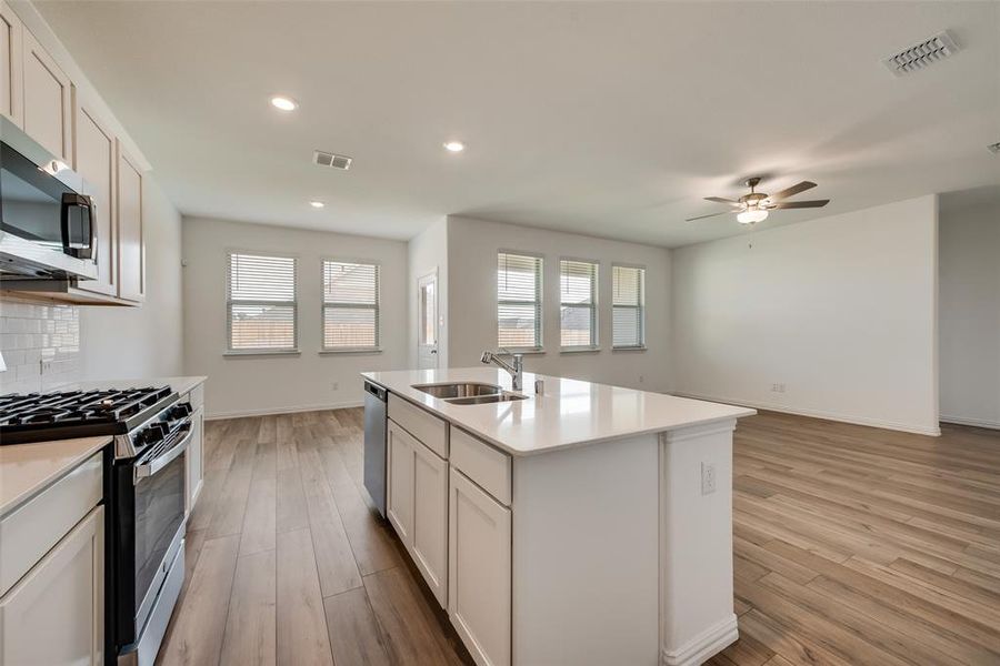 Kitchen with an island with sink, light hardwood / wood-style flooring, backsplash, and appliances with stainless steel finishes