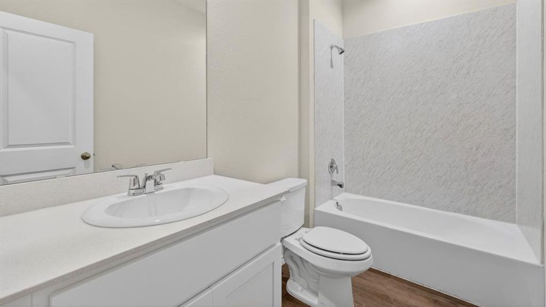 Bathroom featuring a white vanity with an integrated sink and chrome faucet, a large mirror, a white toilet, and a bathtub with a textured surround