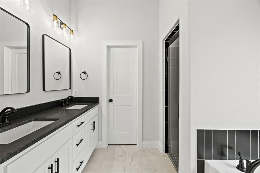 Full bathroom with double vanity, light marble finish floors, and a tub