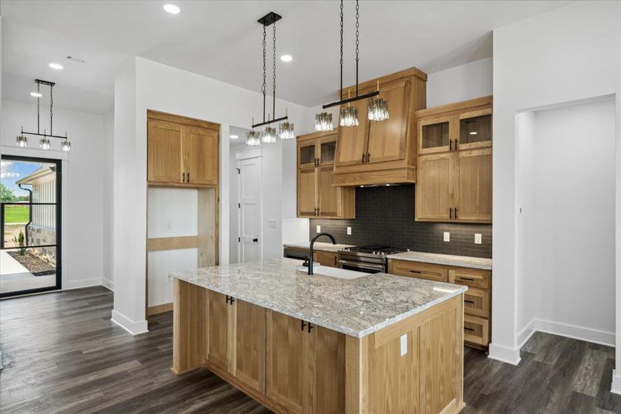 Kitchen with stainless steel gas range oven, an island with sink, tasteful backsplash, dark wood-style flooring, and light stone counters