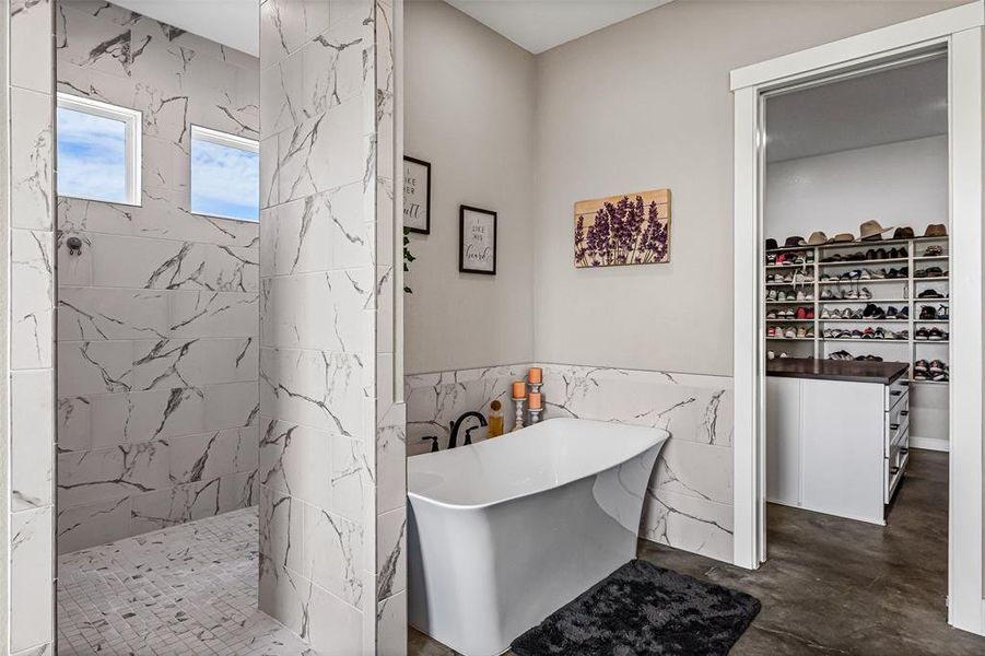 Bathroom featuring a wainscoted wall, tile walls, a marble finish shower, a freestanding tub, and a walk in closet Bathroom featuring a wainscoted wall, tile walls, a marble finish shower, a freestanding tub, and a walk in closet