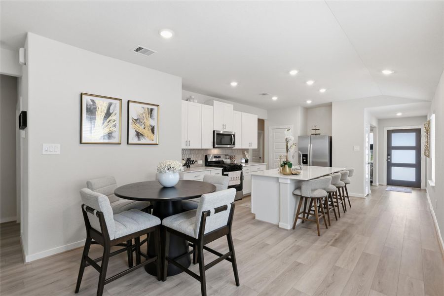 This photo showcases a modern, open-concept kitchen and dining area with sleek white cabinetry, stainless steel appliances, and a large island with bar seating. The space features light wood flooring and ample natural light, creating a bright and inviting atmosphere.