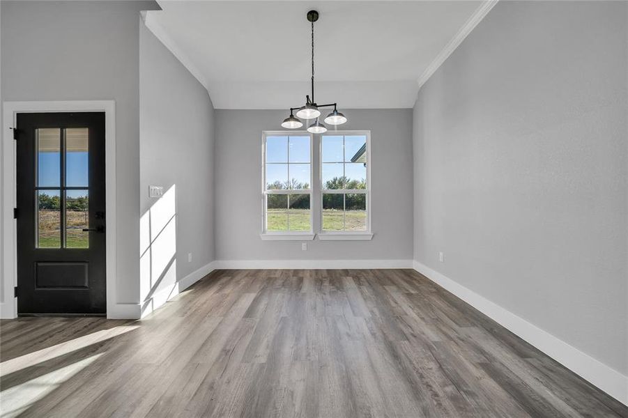 Unfurnished dining area featuring wood-type flooring, a notable chandelier, a healthy amount of sunlight, and crown molding