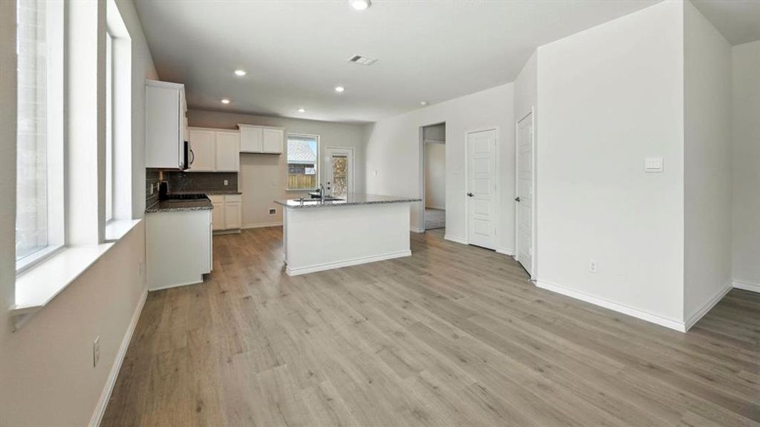 Kitchen with white cabinetry, a center island with sink, tasteful backsplash, dark stone counters, and light wood-style floors