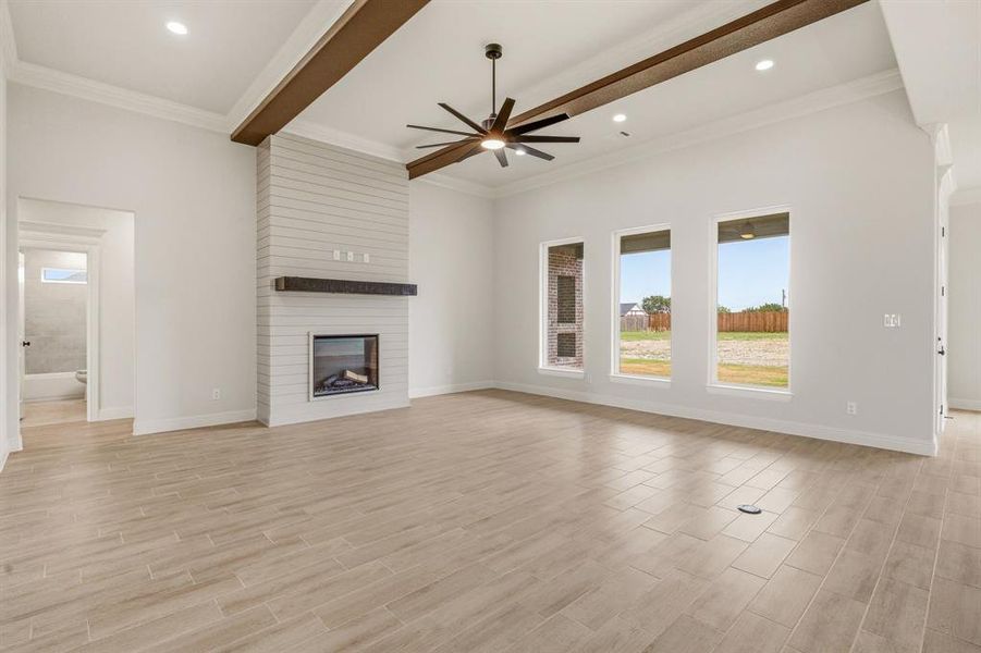 Unfurnished living room featuring a ceiling fan, a large fireplace, healthy amount of natural light, ornamental molding, and wood finish floors