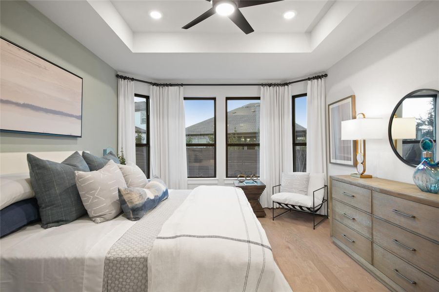 Bedroom featuring a tray ceiling, light wood-type flooring, multiple windows, and recessed lighting