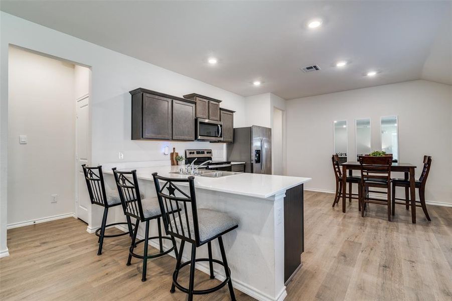 Kitchen with a breakfast bar area, a sink, visible vents, light countertops, and appliances with stainless steel finishes