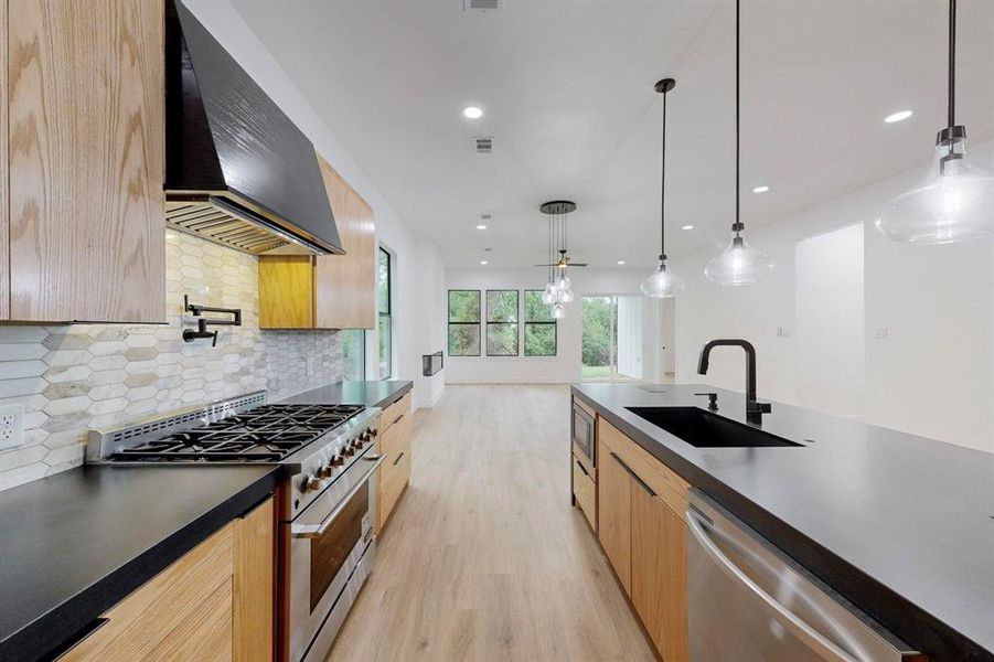 Modern kitchen featuring light wood-finish cabinetry, dark countertops, and a full stainless steel range with a pot filler faucet Modern kitchen featuring light wood-finish cabinetry, dark countertops, and a full stainless steel range with a pot filler faucet