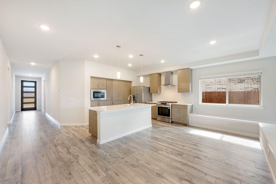 Open-concept kitchen with large island, tan cabinets, stainless steel appliances, and light wood floors