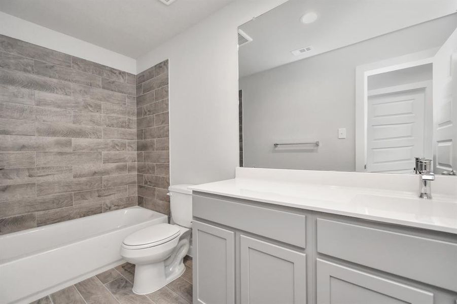 Indulge in refined charm in the secondary bathroom, where the tile flooring harmonizes with a bath/shower combo surrounded by tasteful tile. Sample photo of completed home with similar floor plan. As-built interior colors and selections may vary.