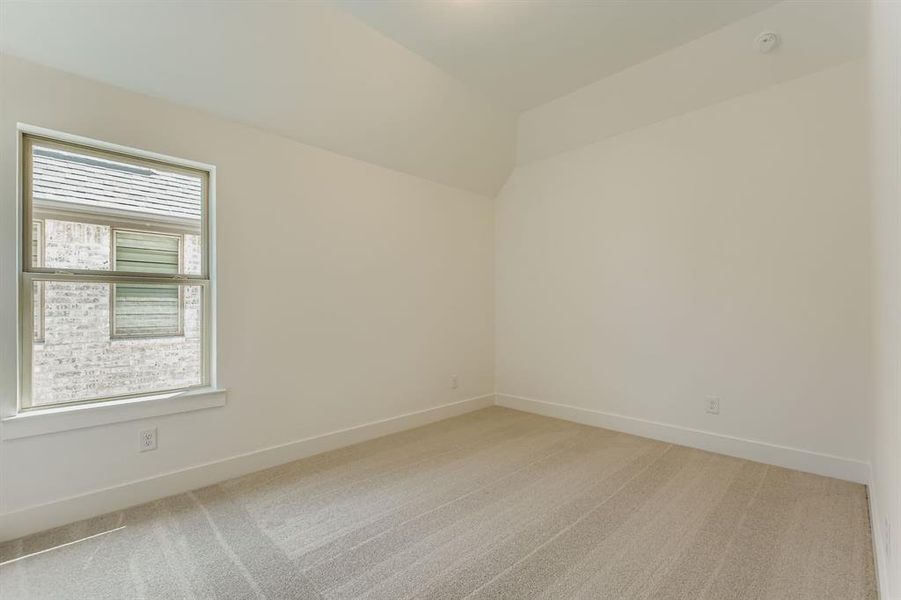 Empty room with light carpet, lofted ceiling, and a smoke detector Empty room with light carpet, lofted ceiling, and a smoke detector