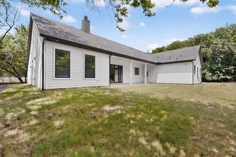 Expansive backyard featuring a white siding exterior with a dark-pitched roof, black-framed windows, and a covered patio area