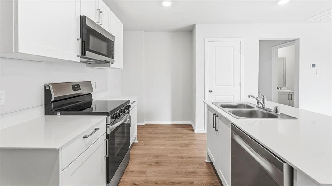 Kitchen featuring stainless steel appliances, light wood-style flooring, white cabinetry, an island with sink, and recessed lighting Kitchen featuring stainless steel appliances, light wood-style flooring, white cabinetry, an island with sink, and recessed lighting