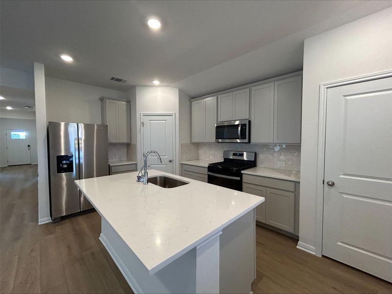 Kitchen with tasteful backsplash, dark wood-style flooring, appliances with stainless steel finishes, gray cabinets, and light stone counters Kitchen with tasteful backsplash, dark wood-style flooring, appliances with stainless steel finishes, gray cabinets, and light stone counters