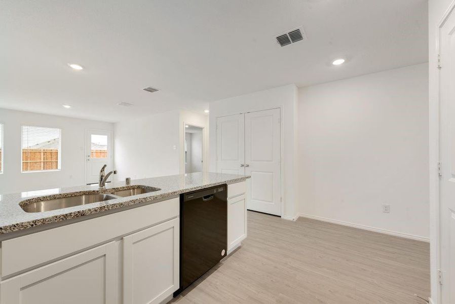 Kitchen featuring light stone counters, visible vents, white cabinetry, a sink, and dishwasher