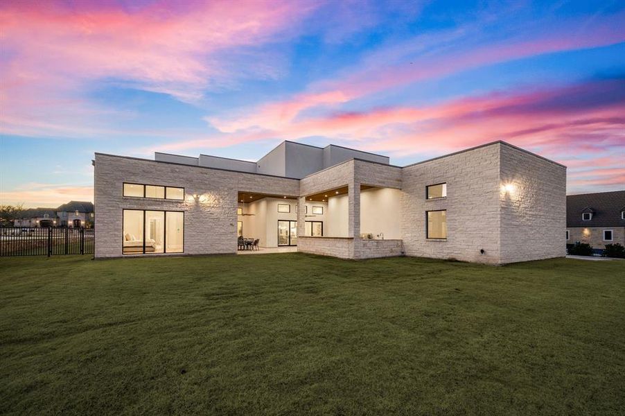 Back house at dusk with a yard and a patio