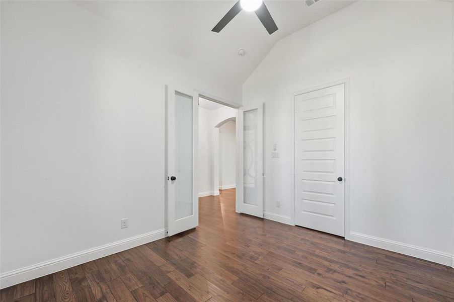 Unfurnished bedroom featuring vaulted ceiling, dark wood-style floors, ceiling fan, and arched walkways