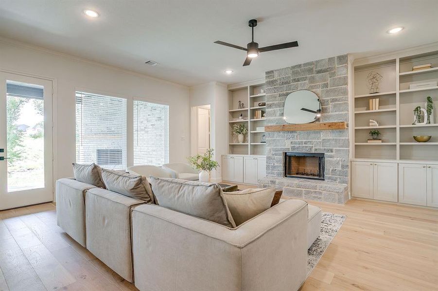 Living area with built in adjustable shelves, light engineered wood flooring, a stone fireplace with solid cedar mantle, ceiling fan, and french doors that open to a covered back patio. Living area with built in adjustable shelves, light engineered wood flooring, a stone fireplace with solid cedar mantle, ceiling fan, and french doors that open to a covered back patio.