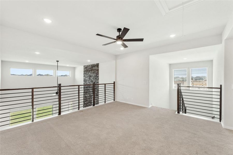 Open upstairs loft with carpet, ceiling fan, metal railing, and stone accent wall