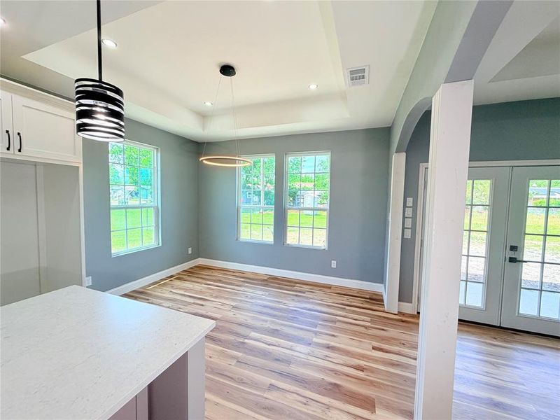 Spacious interior featuring wood-finish flooring, a tray ceiling with recessed lighting, and contemporary pendant fixtures