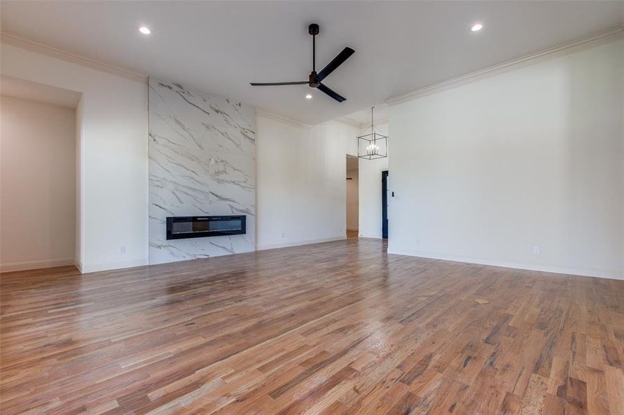 Unfurnished living room with light wood-type flooring, ceiling fan with notable chandelier, a premium fireplace, and crown molding