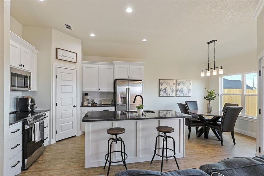 Open-concept kitchen and dining area featuring white cabinetry, dark countertops, stainless steel appliances, a kitchen island with seating, and wood-finish flooring