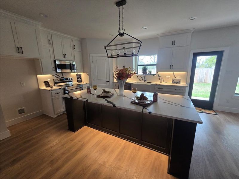 Kitchen featuring hanging light fixtures, stainless steel appliances, light stone countertops, a kitchen island, and light wood finished floors