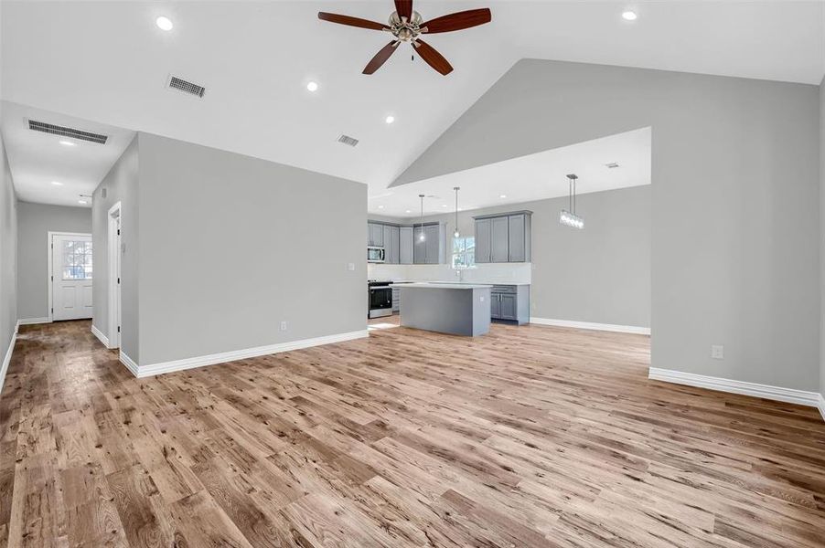 Unfurnished living room with ceiling fan, high vaulted ceiling, and light hardwood / wood-style flooring