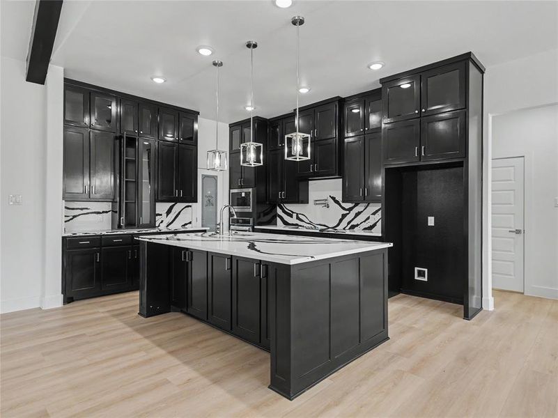 Gourmet kitchen featuring a large central island with integrated sink, black cabinetry with glass-front uppers, white countertops, and a striking black and white backsplash Gourmet kitchen featuring a large central island with integrated sink, black cabinetry with glass-front uppers, white countertops, and a striking black and white backsplash