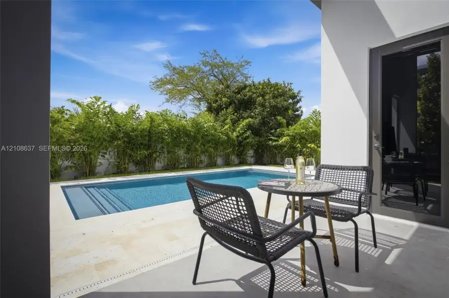 Private swimming pool with integrated stairs, expansive light-toned stone decking, and tall perimeter privacy landscaping
