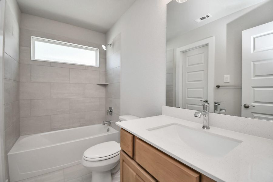 Secondary bath features tile flooring, bath/shower combo with tile surround, light stained wood cabinets, beautiful light countertop. Sample photo of completed home with similar floor plan. Actual colors and selections may vary.