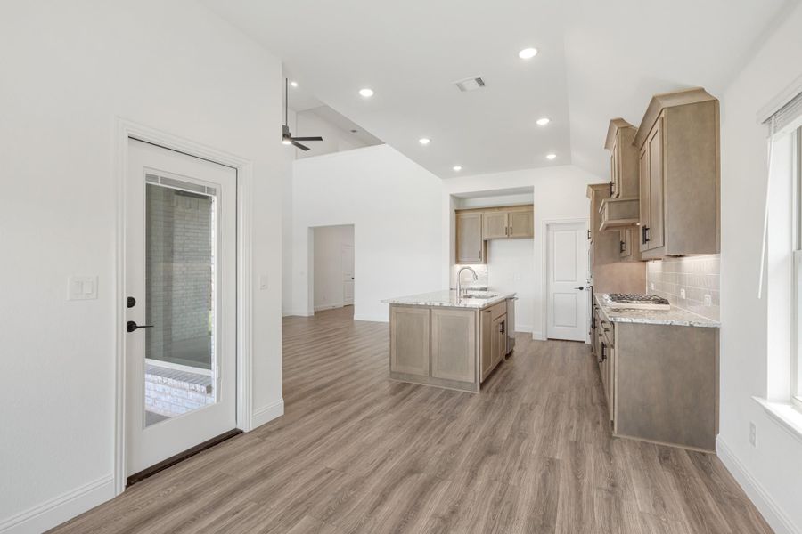 Open kitchen with tan cabinets, center island, granite countertops, and wood-look floors Open kitchen with tan cabinets, center island, granite countertops, and wood-look floors
