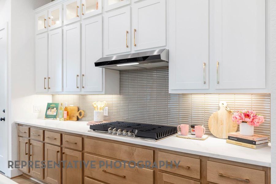 Kitchen with stainless steel gas cooktop, under cabinet range hood, light countertops, tasteful backsplash, and glass insert cabinets Kitchen with stainless steel gas cooktop, under cabinet range hood, light countertops, tasteful backsplash, and glass insert cabinets